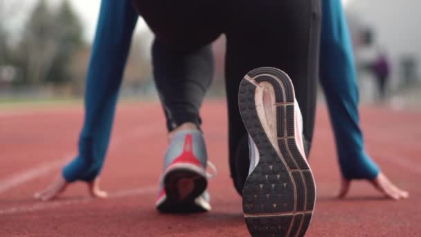 Vista trasera de un joven atleta preparándose para la carrera en una pista de carreras . — Vídeos de Stock