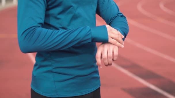 Vista de cerca, hombre corredor mirando reloj inteligente en el estadio. Joven atleta comprobando resultados en smart watch en pista de atletismo . — Vídeos de Stock