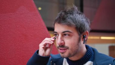 Şehir arka planında dikilirken kablosuz kulaklık takan yakışıklı genç adam..