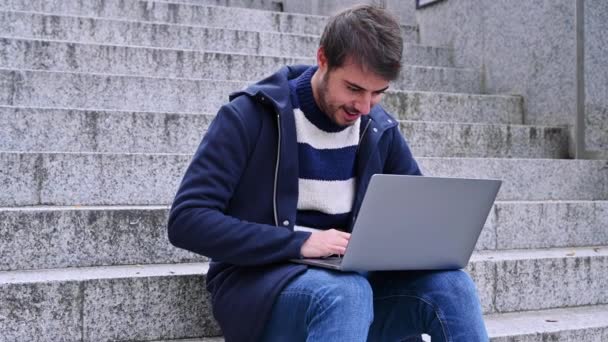 Young bearded businessman sits on steps, using laptop and looks on his screen. Hipster man is working, blogging, chatting online,checking email. Student learning online. Summer sunny day. Lifestyle. — Stock Video