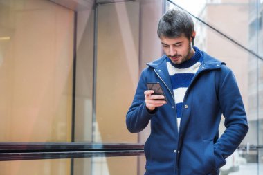 Yakışıklı genç adam, ofis binasının dışında duruyor, işte mola verirken sosyal ağları cep telefonunda kullanıyor..