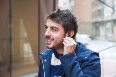 Yakışıklı genç adam, yürürken kablosuz kulaklık takıyor, şehir arka planı..