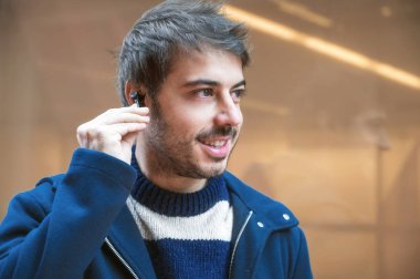 Yakışıklı genç adam, yürürken kablosuz kulaklık takıyor, şehir arka planı..