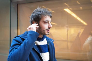 Yakışıklı genç adam, yürürken kablosuz kulaklık takıyor, şehir arka planı..