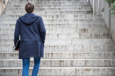 Bilgisayarı elinde tutan genç adam merdivenlerden yukarı çıkıyor..