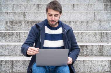 Yakışıklı hippi modern iş adamı, şehirde dizüstü bilgisayar kullanıyor, pozitif ifadeli..