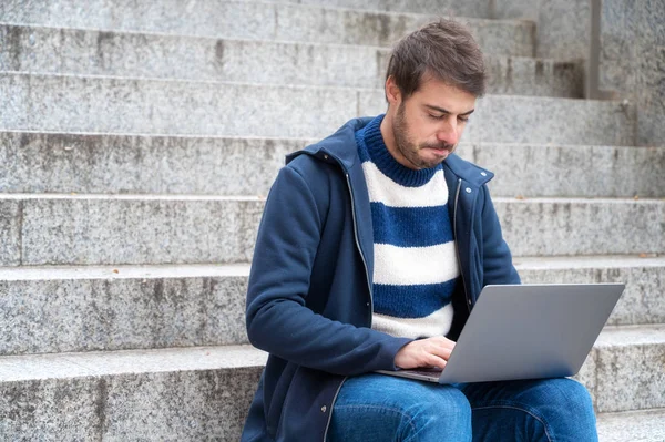 Young serious expression, man freelancer working with laptop outdoors sitting at stair steps, in urban scenery. — Stock Photo, Image