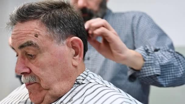 Barbeiro aparar o cabelo do homem velho na barbearia . — Vídeo de Stock