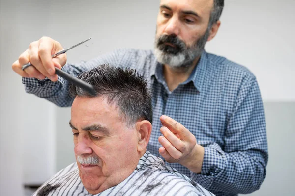 Kapper trimmen haar van oude man bij kapperszaak. — Stockfoto