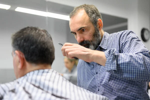 Kapper trimmen haar van oude man bij kapperszaak. — Stockfoto