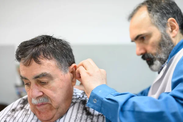 Kapper trimmen haar van oude man bij kapperszaak. — Stockfoto