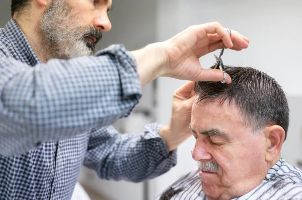 Kapper trimmen haar van oude man bij kapperszaak. — Stockfoto