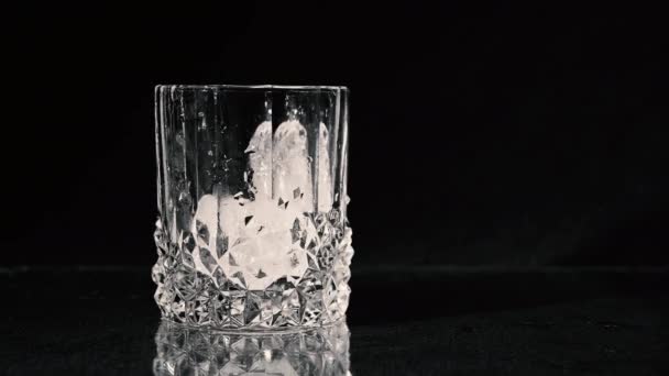 Dropping ice cubes. Whiskey Being Poured Into A Glass on Black Background. Close Up. — Stok video