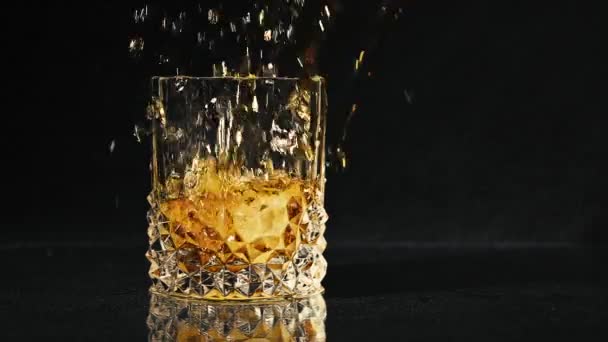 Ice dropped into glass of whisky splashing in slow motion. — Stock Video