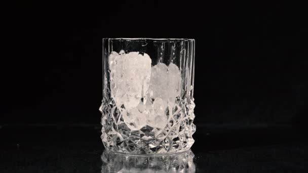 Tirando cubitos de hielo. Whiskey se vierte en un vaso sobre fondo negro. Primer plano . — Vídeo de stock