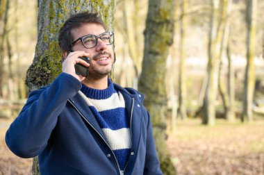 Smiling man, talking on mobile phone in an autumn park.