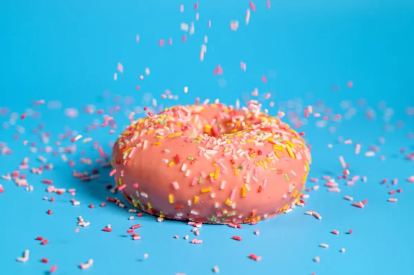 Polvilhas caindo de cima no saboroso donut de morango rosa. Deliciosa sobremesa no fundo azul . — Fotografia de Stock