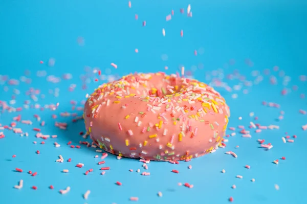 Polvilhas caindo de cima no saboroso donut de morango rosa. Deliciosa sobremesa no fundo azul . — Fotografia de Stock