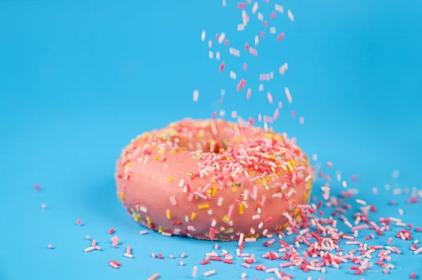 Polvilhas caindo de cima no saboroso donut de morango rosa. Deliciosa sobremesa no fundo azul . — Fotografia de Stock