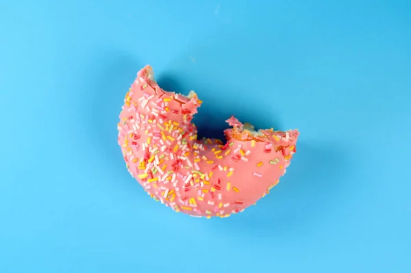 Donut fosco rosa com polvilhas coloridas com falta de mordida. No fundo azul . — Fotografia de Stock