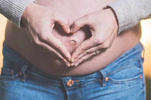 Le mani della donna incinta che fanno forma di cuore sulla pancia . — Foto Stock