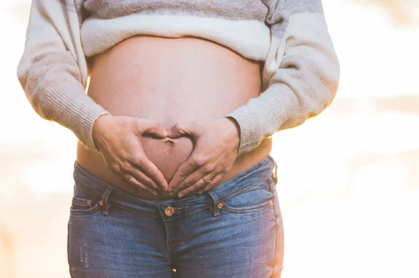 Le mani della donna incinta che fanno forma di cuore sulla pancia . — Foto Stock