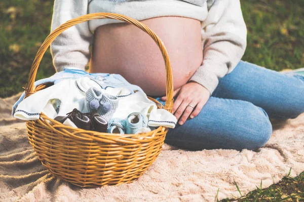 Donna incinta in attesa di un bambino, in posa all'aperto con un cesto di vimini con vestiti per il suo neonato . — Foto Stock