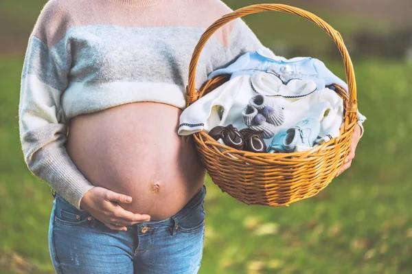 Donna incinta in attesa di un bambino, in posa all'aperto con un cesto di vimini con vestiti per il suo neonato . — Foto Stock
