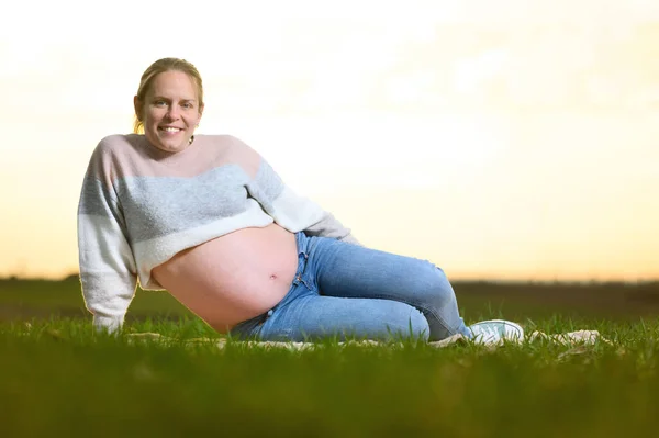 Bella donna incinta sdraiata sul parco al tramonto. All'aperto incinta ritratto . — Foto Stock