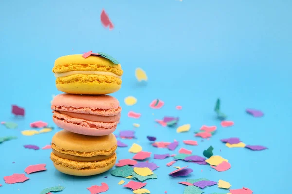 Macarons coloridos no papel azul pastel na moda com confete. saborosos macaroons rosa, amarelo e marrom . — Fotografia de Stock