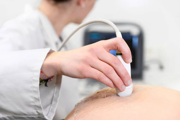 Un médecin fait une échographie ou une échographie à une femme enceinte à l'hôpital, plan rapproché du transducteur en mouvement de l'obstétricien sur le ventre de la future mère . — Photo