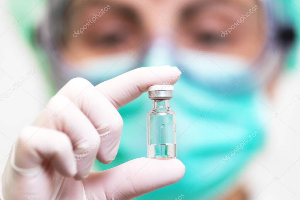 A doctor in medical gloves and mask holding an ampula with vaccine. Close up shot. Coronavirus, epidemic and medicine concept.