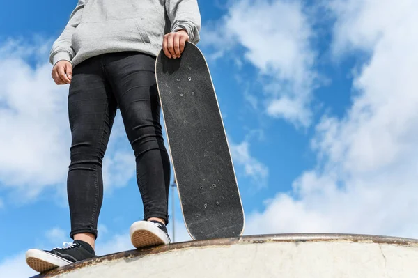 Gros plan d'un jeune homme méconnaissable tenant du skateboard dans le parc sur fond de ciel bleu . — Photo