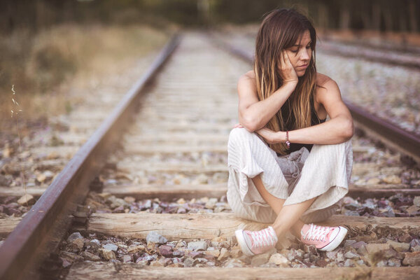 Портрет молодой грустной женщины, сидящей задумчивой на открытом воздухе на железнодорожном пути
.