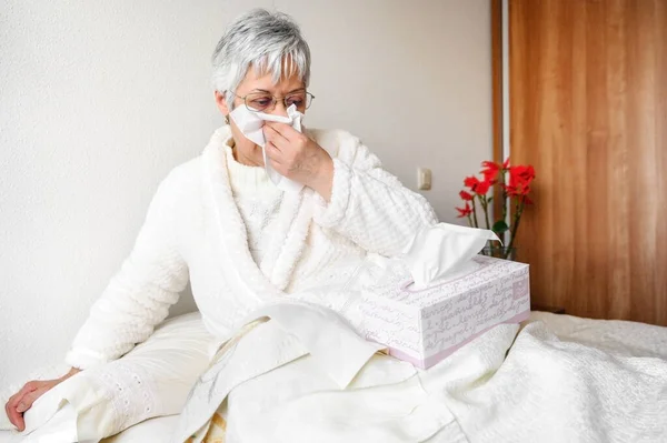 Pandemia koronawirusa. Opieka zdrowotna, grypa, higiena i koncepcja ludzi. Chora starsza kobieta z papierową chusteczką dmuchająca mu nos w domu. — Zdjęcie stockowe