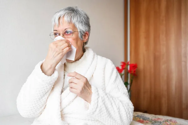 Pandemia koronawirusa. Opieka zdrowotna, grypa, higiena i koncepcja ludzi. Chora starsza kobieta z papierową chusteczką dmuchająca mu nos w domu. — Zdjęcie stockowe
