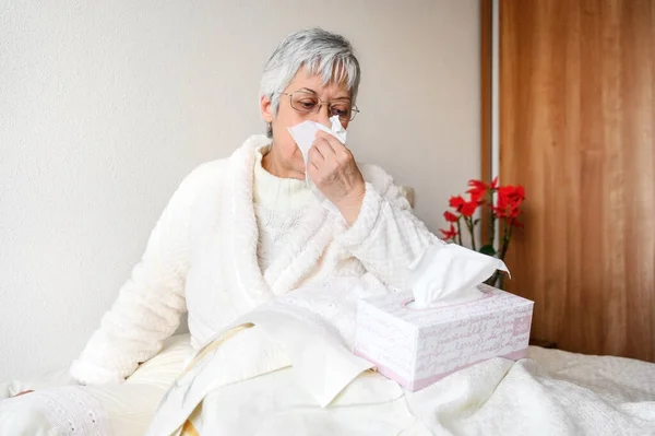 Pandemia koronawirusa. Opieka zdrowotna, grypa, higiena i koncepcja ludzi. Chora starsza kobieta z papierową chusteczką dmuchająca mu nos w domu. — Zdjęcie stockowe