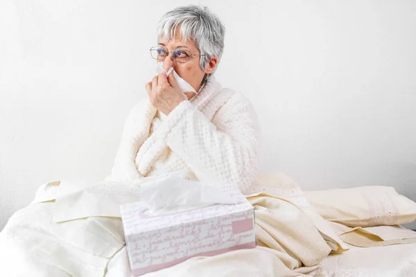 Coronavirus pandemic. Healthcare, flu, hygiene and people concept. Sick senior woman with paper wipe blowing his nose at home. — Stock Photo, Image