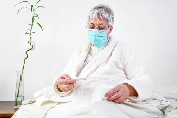 Covid-19. Sick senior woman in bed, wearing face protection mask, fever and coughing, pneumonia disease, risk patient, flu and cold. — Stock Photo, Image