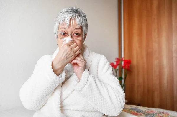 Coronavirus pandemic. Healthcare, flu, hygiene and people concept. Sick senior woman with paper wipe blowing his nose at home. — Stock Photo, Image