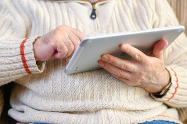 Kanepede oturan ve oturma odasında dijital tablet kullanan yaşlı adamın portresini kapat..