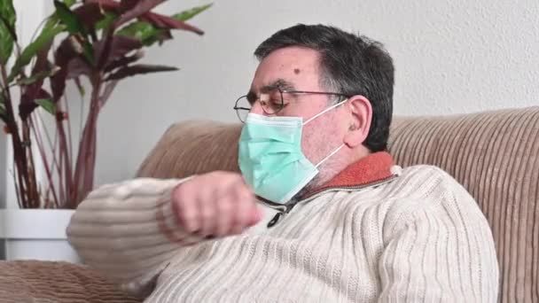 Пожилой мужчина с симптомами коронавируса кашляет ей в рукав или локоть, чтобы предотвратить распространение Ковида-19. Корона вирус, больной пожилой человек в защитной маске, чихающий закрывающий нос, рот рукой . — стоковое видео