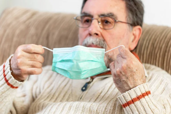 Starszy mężczyzna zakłada maskę medyczną na twarz, by chronić się przed pandemią koronawirusa.. — Zdjęcie stockowe