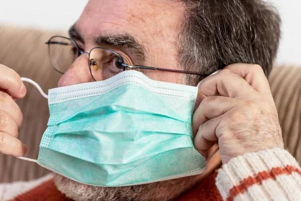 Starszy mężczyzna zakłada maskę medyczną na twarz, by chronić się przed pandemią koronawirusa.. — Zdjęcie stockowe