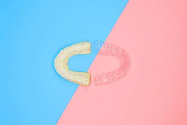 Molde de gesso dental e treinador de silicone ortodôntico. Aparelho ortodôntico móvel para correção dentária, em fundo azul e rosa . — Fotografia de Stock