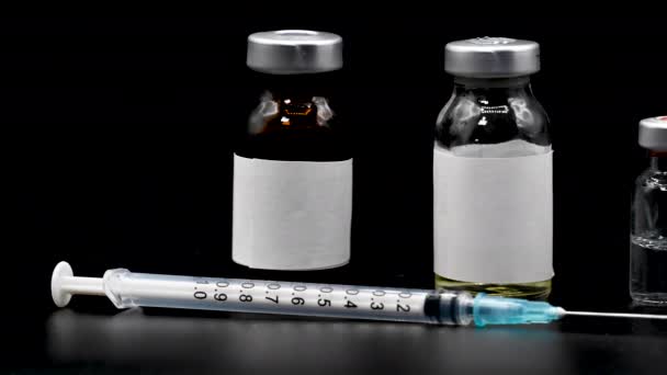 Coronavirus pandemic, people vaccination concept. Vaccine syringe with vials, medicines close up on black background , dolly shot left to right. — Stock Video