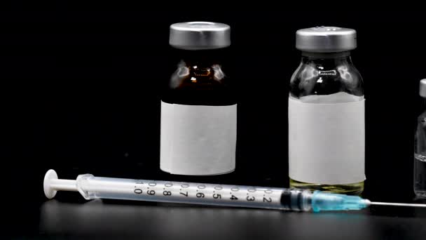 Koronavirová pandemie, koncepce očkování lidí. Vakcinační stříkačka s injekčními lahvičkami, léky zblízka na černém pozadí, panenka zleva doprava. — Stock video