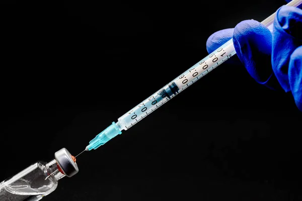 검은 색 배경에서 백신 접종을 위해 주사기와 유리병을 준비하는 의사의 손을 클로즈업. — 스톡 사진