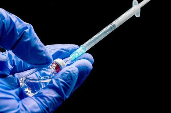 검은 색 배경에서 백신 접종을 위해 주사기와 유리병을 준비하는 의사의 손을 클로즈업. — 스톡 사진