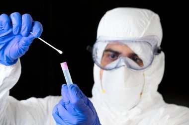 Sağlık teknolojisi uzmanı elinde COVID-19 bez toplama seti tutuyor, beyaz PPE koruyucu kıyafet maske eldivenleri giyiyor, hasta numune almak için test tüpü kullanıyor..
